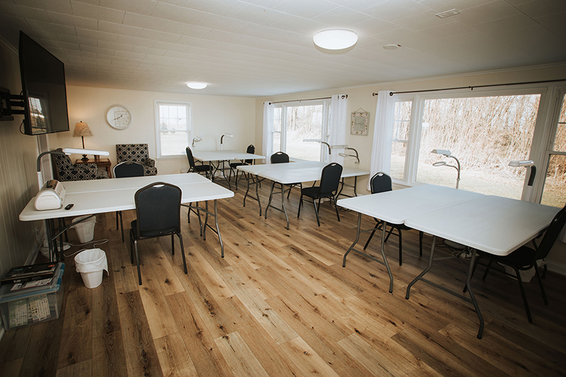 Picture of the inside of Grandma's House at Circle K Farm, where a large open room is decorated with plastic tables and chairs and a spacious view of the outdoors, complete with two reclining chairs, a lamp, and a flat-screen television